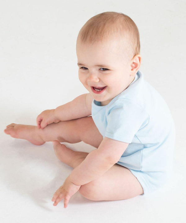 A baby in a light blue Larkwood LW55T sits on the floor, smiling and reaching out with its right hand while its legs are bent.