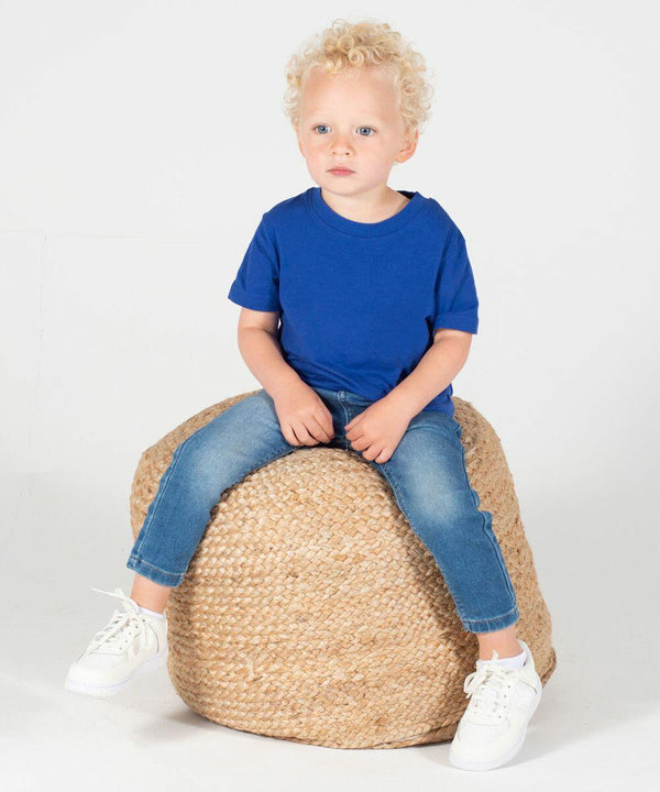 A young child with curly blonde hair wearing a blue t-shirt, jeans, and white sneakers sits on a woven pouf against a plain white background, modeling the LW620 from Larkwood.
