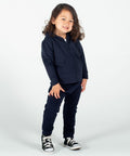 A child with long hair stands smiling, wearing a navy blue Larkwood LW62T hoodie and matching pants, with black and white sneakers against a plain white background.