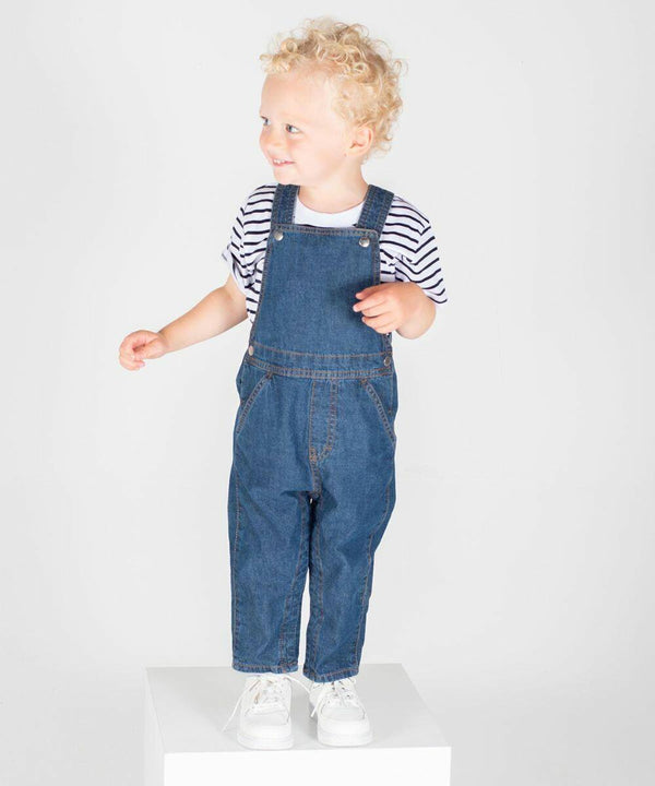 A toddler with curly blonde hair is wearing blue denim overalls, a black and white striped t-shirt, and white sneakers. The child stands on a white platform against a plain background in the Larkwood LW700.