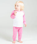 A young child with blonde hair is standing barefoot, wearing a white and pink long-sleeve shirt and pink pants from Larkwood, looking slightly upwards.