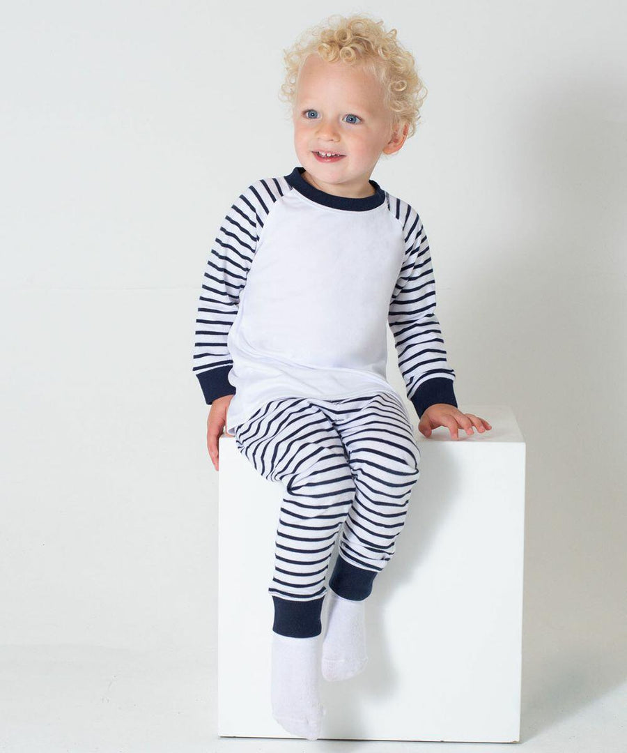 A young child with curly hair, dressed in Larkwood LW72T pajamas, sits on a white cube against a plain background.