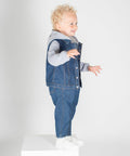 A young child with curly blond hair is standing on a white box, wearing a gray Larkwood LW750 hoodie under a blue denim vest and blue jeans. The child is looking to the right and smiling.