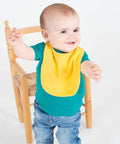A baby wearing a yellow bib and teal shirt, stands and stretches arms out near a Larkwood LW82T.