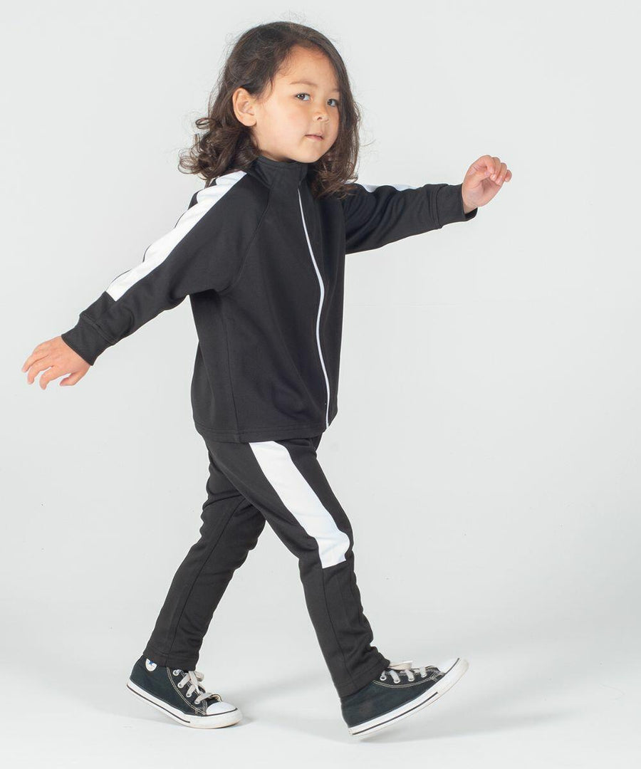 A child with medium-length hair walks forward wearing a Larkwood LW830 black tracksuit with white stripes and black sneakers against a plain background.