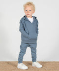 A young child with curly hair stands on a carpet wearing a blue Larkwood LW850 hoodie, matching pants, and white sneakers, looking slightly to the side.