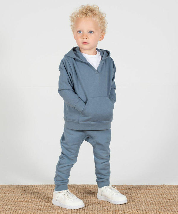 A young child with curly hair stands on a carpet wearing a blue Larkwood LW850 hoodie, matching pants, and white sneakers, looking slightly to the side.