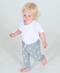 A toddler with blond hair wearing a white LW85T Larkwood shirt and gray star-patterned pants walks barefoot on a white background.