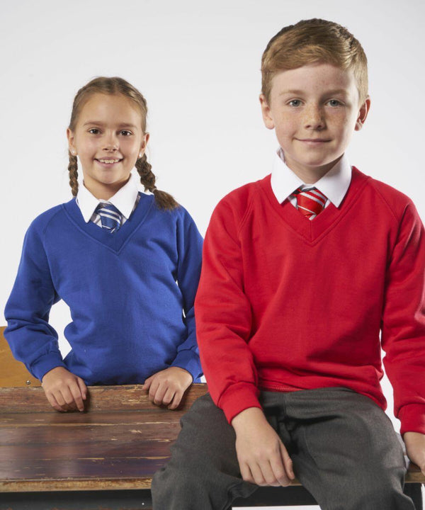 Two children sitting on a bench, dressed in school uniforms; the girl wears a blue MD02B Maddins sweater and tie, while the boy wears a red MD02B Maddins sweater and tie. Both are smiling and looking at the camera.