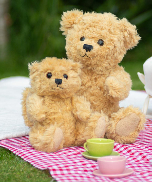 Two Mumbles MM016 teddy bears sitting on a red and white checkered blanket outdoors with small green and yellow teacups in front of them.