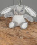 A small, gray and white MM023 by Mumbles with long ears sits on a wooden surface.
