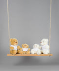 Four Mumbles MM030 teddy bears of different sizes, each wearing a white shirt, sit on a wooden swing against a plain gray background.