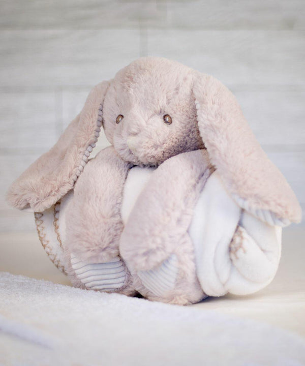 A soft, plush bunny toy with long ears and a round body wrapped in a white blanket, placed on a light-colored surface, MM034 by Mumbles.