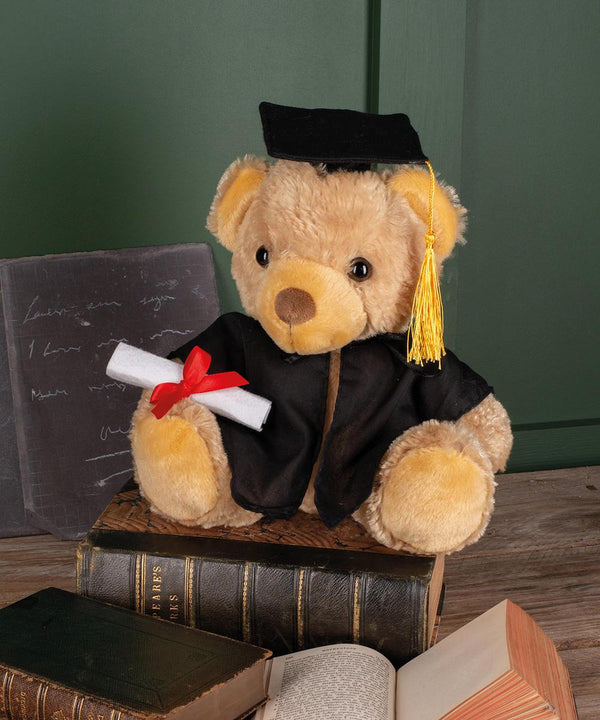 The Mumbles Graduation bear wears a black cap and gown, holds a rolled diploma with a red ribbon, and sits on stacked books, with an open book and blackboard featured in the background.