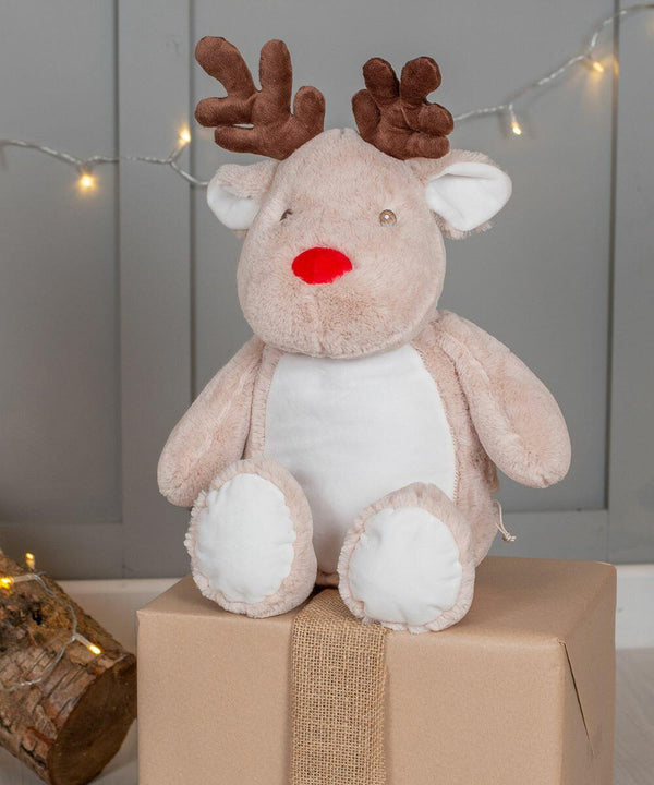 A Mumbles MM560 with brown antlers, a red nose, and a white belly sits on a wrapped gift box in front of a gray wall and string lights.