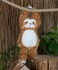 A Mumbles MM572 hangs by its arms from a thick rope in front of a bamboo backdrop, with green plants and wooden blocks surrounding it.