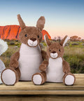 Two Mumbles MM575 toys are sitting on a wooden surface with a natural landscape and large rock formation in the background.