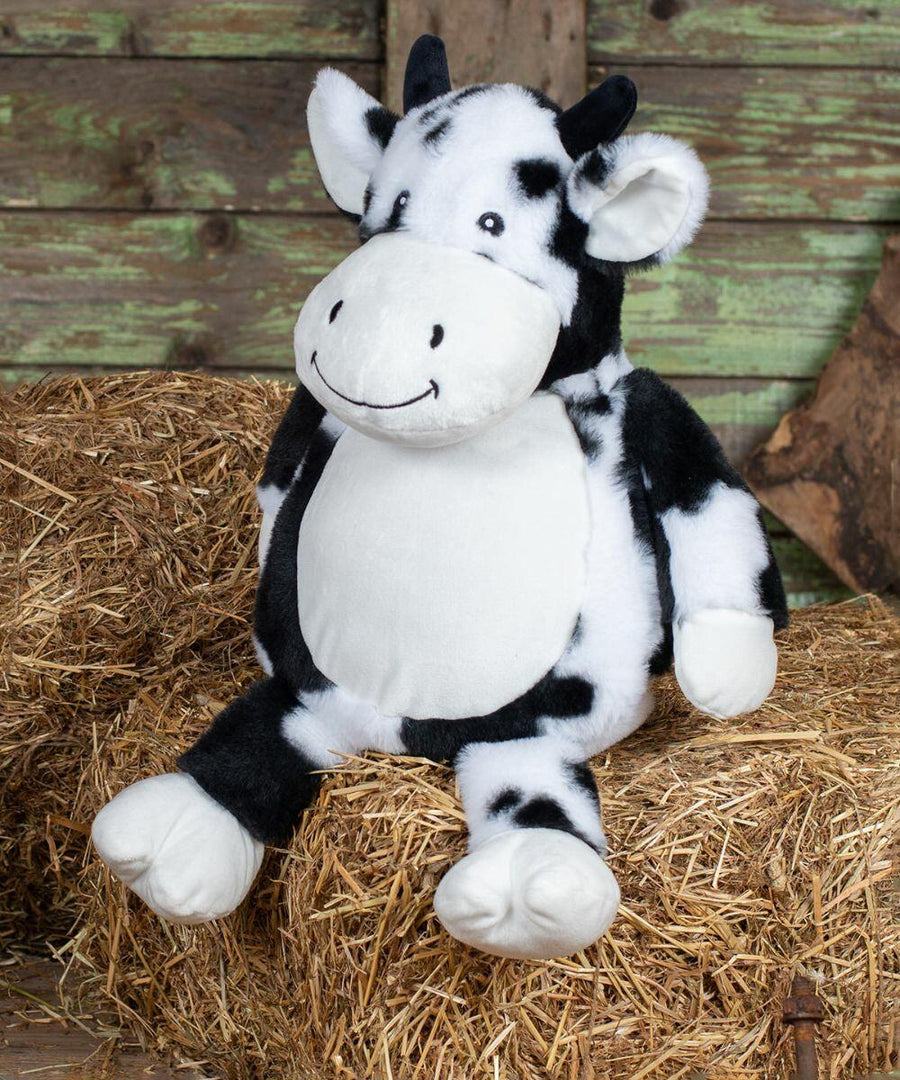 A Mumbles MM578 with black and white patches is seated on a bale of hay in front of a wooden backdrop.