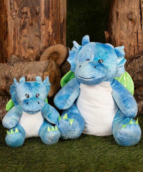 Two plush blue dragon toys sit on grass with wooden logs in the background. The larger dragon has green wings and spikes, while the smaller one matches with similar features. The product is MM579 from Mumbles.