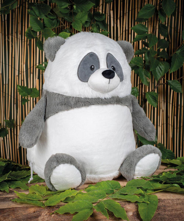 The Mumbles Zippie panda, with soft grey and white fur and an embroidered face, sits on a stone surface amid green plants, with a bamboo screen in the background.