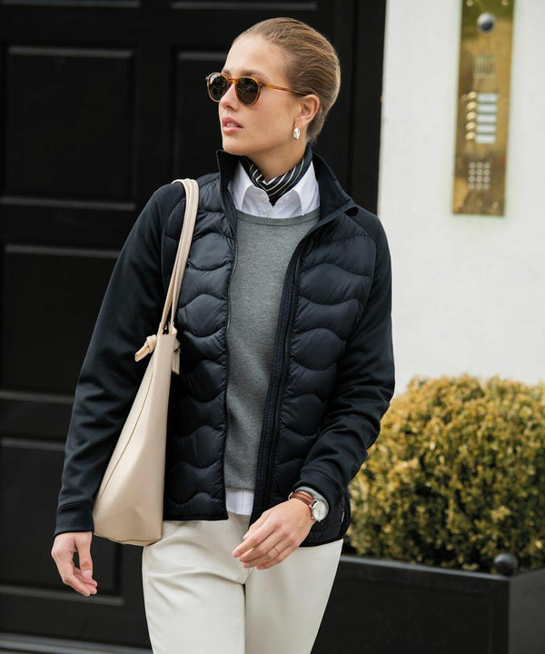 A person wearing sunglasses, a scarf, a black jacket, a grey sweater, a white shirt, and beige pants is carrying a Nimbus N104F while walking outdoors.