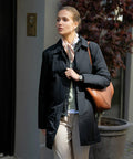 A person wearing a black coat and carrying a Nimbus N105F stands in an outdoor urban area.