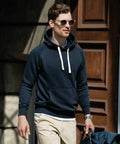 A man wearing sunglasses, a dark hoodie, and light pants holds a Nimbus N106M while walking outside near a wooden door.