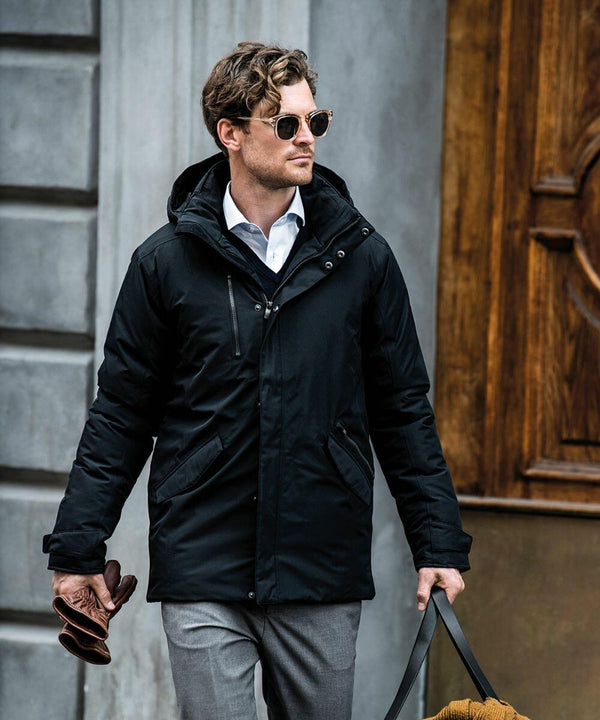 A man wearing a black coat, sunglasses, and carrying a Nimbus N111M walks past a wooden door.