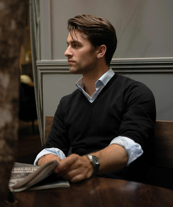 A man with dark hair wearing a black sweater and white shirt sits at a table, holding an N112M by Nimbus and looking to the side.