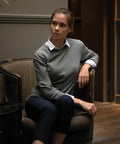 A woman sits on a vintage-style Nimbus N113F armchair, wearing a gray sweater over a white shirt and dark pants, with her right arm resting on the chair's armrest.