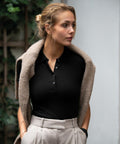 A woman wearing a black Nimbus N119F polo shirt, light-colored trousers, and a beige cardigan draped over her shoulders stands outdoors.