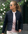 Person with sunglasses and ponytail wearing a navy jacket and holding a Nimbus N122F stands outdoors near rose bushes.