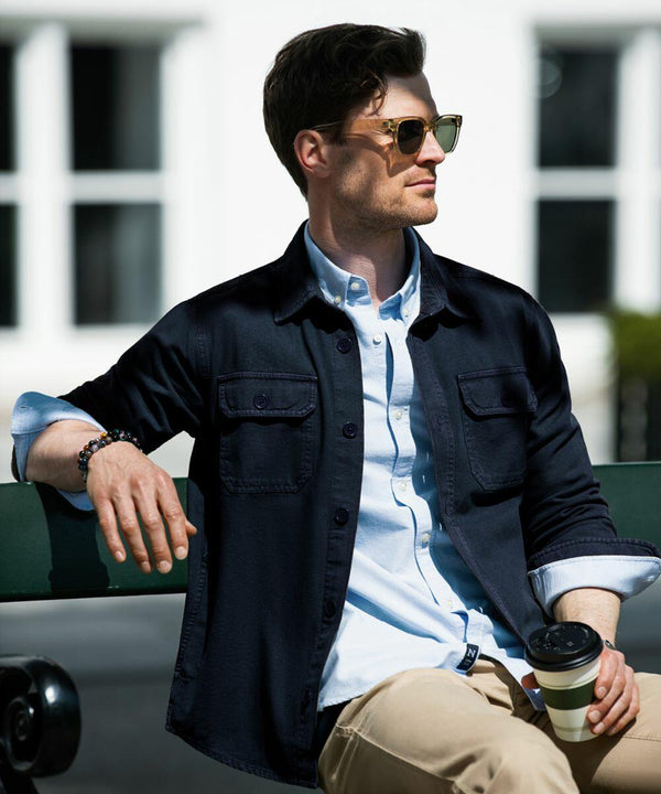 A person with short hair and sunglasses sits on a bench, wearing a dark jacket over a light shirt, holding a Nimbus NB118.