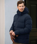 A man wearing a navy Nimbus NB120 puffer jacket and brown gloves stands outdoors, looking to the side.