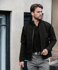 A man wearing a black jacket and gray pants stands outdoors, holding a Nimbus NB30M in his right hand and looking to his left.