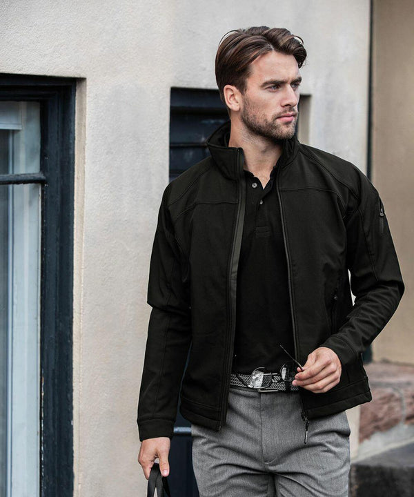 A man wearing a black jacket and gray pants stands outdoors, holding a Nimbus NB30M in his right hand and looking to his left.