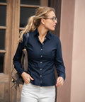 A woman with a ponytail and glasses wearing a navy button-up shirt and white pants is walking while holding a Nimbus NB45F over her shoulder.