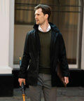 A man wearing a black jacket and grey pants holds a Nimbus NB51M and a folder while standing outside a building.