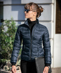 A person wearing a dark puffer jacket and sunglasses is holding a black clutch bag while standing outdoors with their Nimbus NB60F.