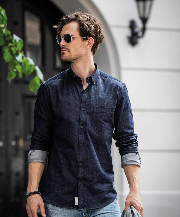 A man wearing sunglasses and a dark denim shirt stands in front of a building, holding a gray NB65M by Nimbus.