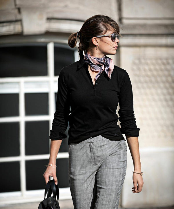 A woman with sunglasses, wearing a black top, gray pants, and a scarf, is holding a Nimbus NB71F while walking in an urban area.