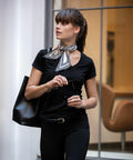 A woman with a ponytail, wearing a black outfit and striped neck scarf, carries a Nimbus NB72F and holds sunglasses, standing near a large window.