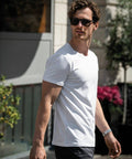 A man wearing Nimbus NB73M sunglasses and a white t-shirt walks outdoors, with plants and a building visible in the background.