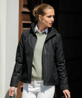 A person wearing a black jacket over a light green Nimbus NB82F and white pants stands outside, looking to the side.