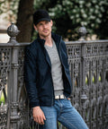 A person wearing a black NB82M jacket and a Nimbus cap leans against a decorative metal fence in an outdoor setting.