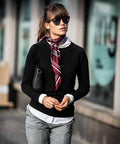 A woman wearing sunglasses, a black top, and a red striped scarf walks on a city sidewalk. She holds a Nimbus NB87F under her arm.