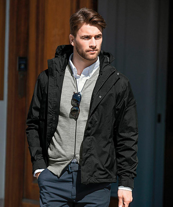 A man wearing a black jacket, light gray sweater, and white dress shirt walks outside with Nimbus NB89M sunglasses hanging from his sweater.