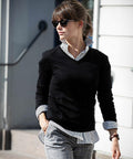 A person wearing sunglasses, a black sweater layered over a striped shirt, and Nimbus NB92F gray plaid pants is walking outdoors.