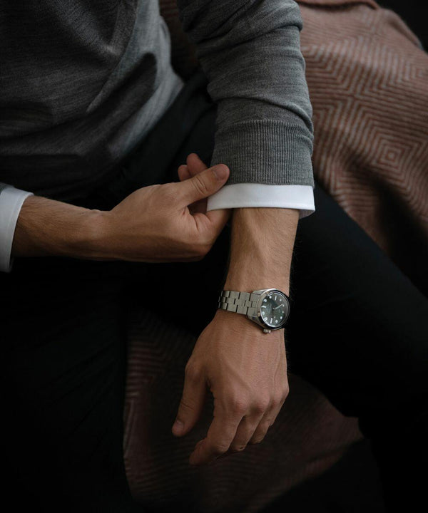 A person is adjusting the sleeve of their gray sweater, while wearing a Nimbus NB92M on their left wrist.