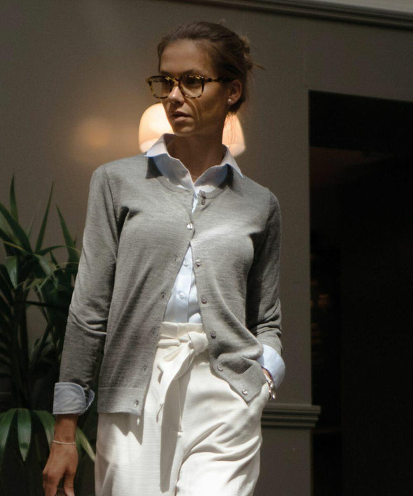 A woman wearing glasses, a light blue shirt, and a gray cardigan stands indoors near a plant, with a Nimbus NB93F in the background.